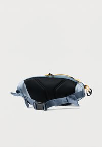 Ανοιχτό μπλε τσαντάκι μέσης με μαύρη επένδυση στο πίσω μέρος, ρυθμιζόμενο λουράκι, κίτρινο φερμουάρ και μαύρο κλιπ, που βρίσκεται επίπεδα πάνω σε λευκό φόντο.