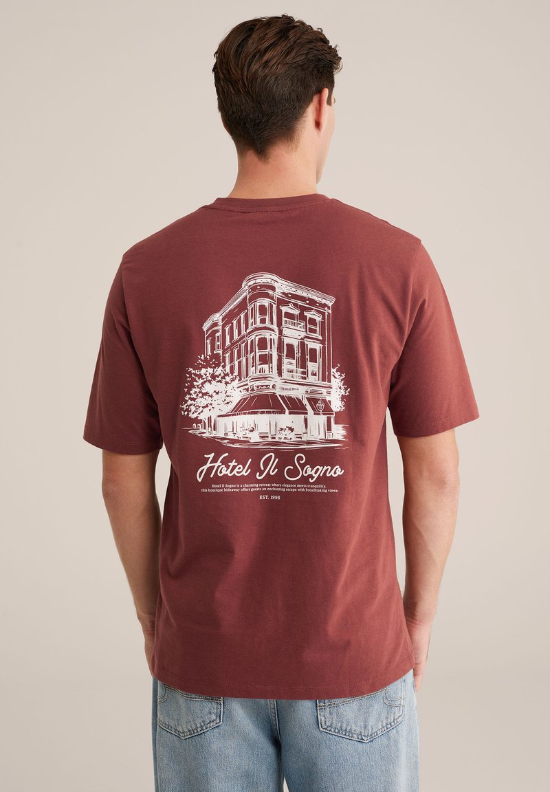 Mørkerød bomulds t-shirt med en hvid grafisk fremstilling af en bygning med træaccentueringer og teksten "Hotel Il Sogno" på ryggen.