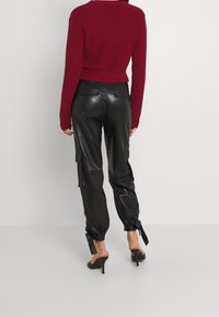 Bordeaux gebreide cropped trui gecombineerd met zwarte neplederen cargobroek met zijzakken en strikken bij de enkels.