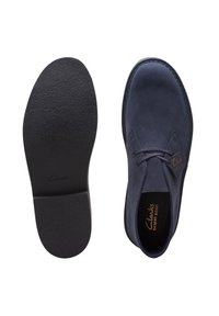 Botas desérticas de ante azul marino con punta redonda, diseño de cordones y suela de goma negra. Presenta el logo dorado de "Clarks" y detalles en cuero.