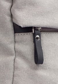 Tessuto grigio con una tessitura testurizzata, caratterizzato da una cerniera scura e un fascetta in pelle. L'accento argento sulla fascetta aggiunge contrasto al design.