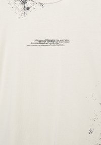 Tricou alb din bumbac, cu text grafic negru și un design cu stropi pe partea stângă. Guler rotund și mâneci scurte.