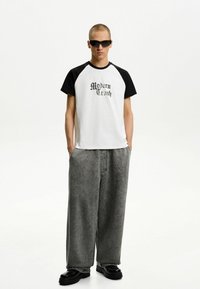 Maglietta bianca e nera con il testo "Modern Crush", abbinata a pantaloni grigi larghi e scarpe nere chunky. Tessuto morbido e vestibilità rilassata.