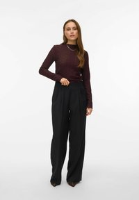 Vinröd långärmad topp med texturerat mönster, kombinerad med svarta vida byxor med hög midja. En enkel halsband förstärker stilen.