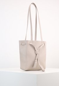 Jasnoszara skórzana torba tote o pudełkowym kształcie, z długimi ramiączkami i detalem w postaci węzła z przodu. Gładka tekstura z minimalną ilością szwów.
