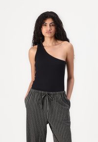 Bodysuit noir à une épaule associé à un pantalon ample noir et crème à rayures, avec une taille élastique et des poches latérales.