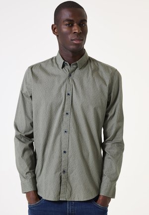 Camisa de botones verde claro con un patrón ondulado, mangas largas, botones azules y cuello estándar, llevada con jeans de mezclilla azules.