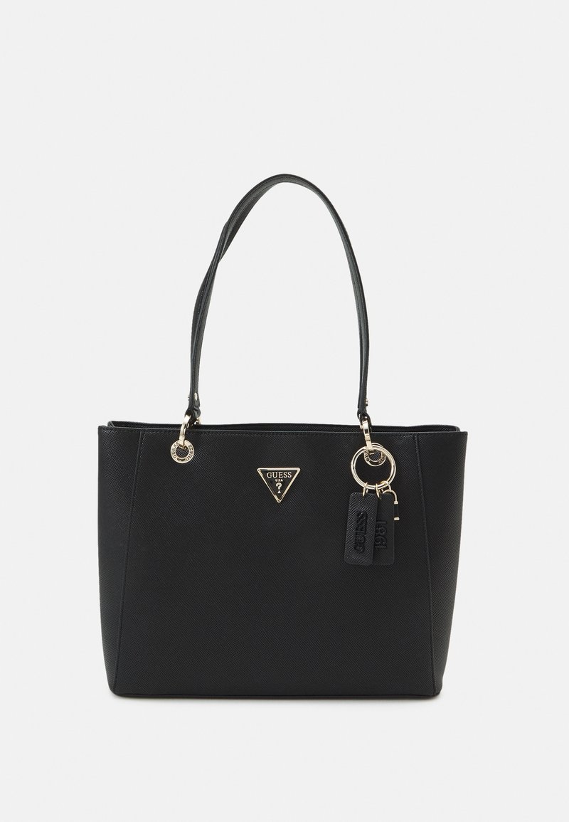 Sac cabas noir Guess avec doubles poignées, garnitures dorées, plaque logo triangulaire et deux porte-clés suspendus sur fond blanc.
