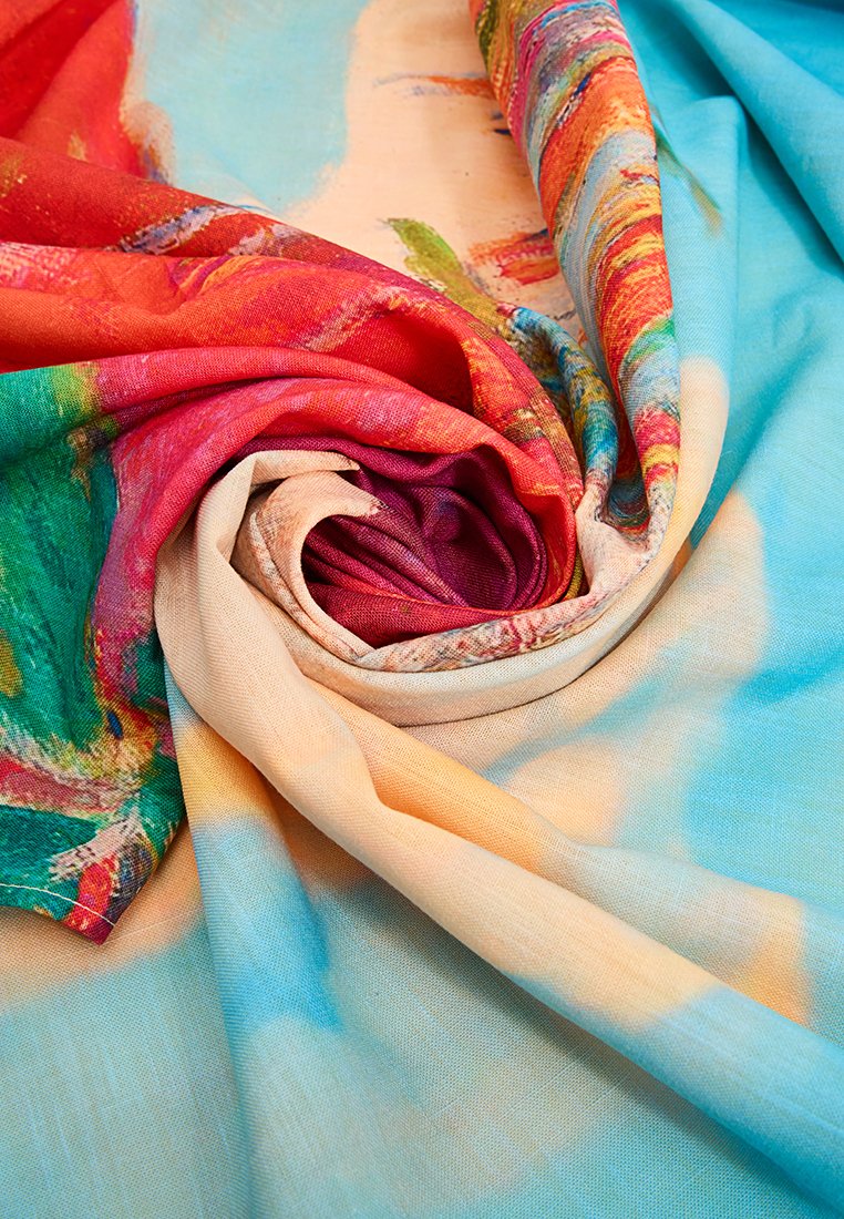 Jasno kolorowa tkanina w odcieniach czerwieni, niebieskiego, zielonego i beżowego, luźno zwinięta w spiralny wzór o różnorodnych fakturach.