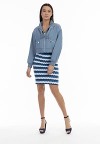 Hellblaues, tailliertes Bomberjacke mit zwei Fronttaschen, kombiniert mit einem blauen und weißen Zickzack-musterierten Bleistiftrock und navyfarbenen High-Heels.