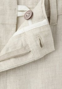 Gros plan sur la ceinture d'un pantalon en lin beige, montrant le bouton, la doublure intérieure blanche, la fermeture éclair et les passants de ceinture.