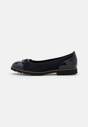 Chaussure plate noire avec bout et talon brillants, corps en daim, petit nœud à l'avant et semelle en caoutchouc rainurée, vue de côté sur fond blanc.
