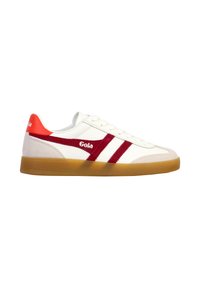 Zapatilla baja blanca con rayas rojas, una lengüeta trasera roja, detalles en ante beige y suela de goma, vista lateral.