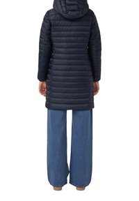 Giacca puffer di un blu scuro con cappuccio, caratterizzata da linee trapuntate orizzontali e una silhouette di lunghezza intermedia, abbinata a pantaloni in denim a gamba larga.