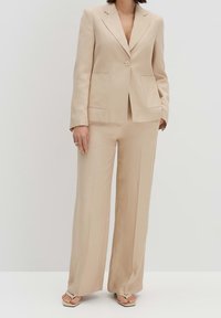 Beige skräddarsydd kostym med en ensam knappblazer och vida byxor, med två framfickor och en mjuk textur.