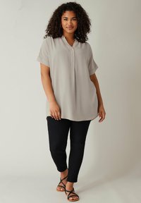 Blusa de manga corta gris claro con un patrón texturizado, cierre de botones y un ajuste relajado, combinada con pantalones ajustados negros y sandalias de tiras.