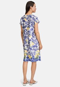 Leichtes Kleid aus Stoff mit floralem und Zitronenmuster in Gelb und Blau. Kurze Ärmel und gerader Schnitt, knielanges Design.