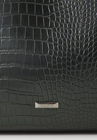 Sac à main en simili cuir noir avec un motif crocodile texturé, présentant une plaque logo métallique ALDO à l'avant. Fini lisse dans l'ensemble.