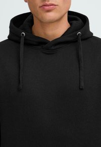 Sudadera negra con cierre de cordón, hecha de una suave mezcla de algodón. Presenta un diseño sencillo y un escote grande y relajado.