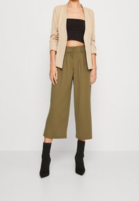 Beżowa marynarka na czarnej bluzce krótkiej, zestawiona z oliwkowymi kulotami. Teksturowane czarne botki za kostkę dopełniają stylizację.