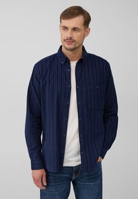 Granatowa koszula zapinana na guziki w pionowe paski, z długim rękawem, kieszonką i klasycznym kołnierzykiem, noszona z białym T-shirtem pod spodem.
