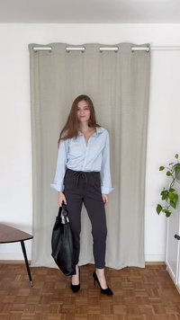 Ανοιχτό μπλε πουκαμίσα, μαύρο παντελόνι σε στένιο σχέδιο με κορδόνι, μαύρη τσάντα και μαύρες ψηλές γόβες, σε ουδέτερο φόντο.