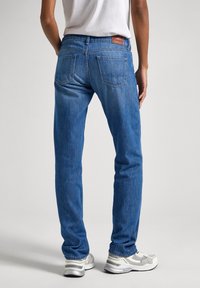 Blå denimjeans med rak passform, med två bakfickor och en läderlapp vid midjan. Bärs med grå och vita sneakers.