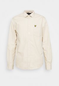 Beige långärmad skjorta med knappar, krage, bröstficka och liten gul fågel-logotyp på fickan.