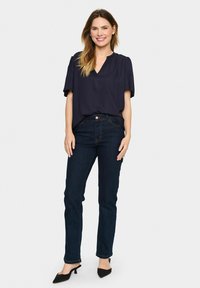 Marinblus med kort ärm och V-ringning, matchad med mörkblå jeans och svarta högklackade skor med spetsig tå. Slät tyg och skräddarsydd passform.