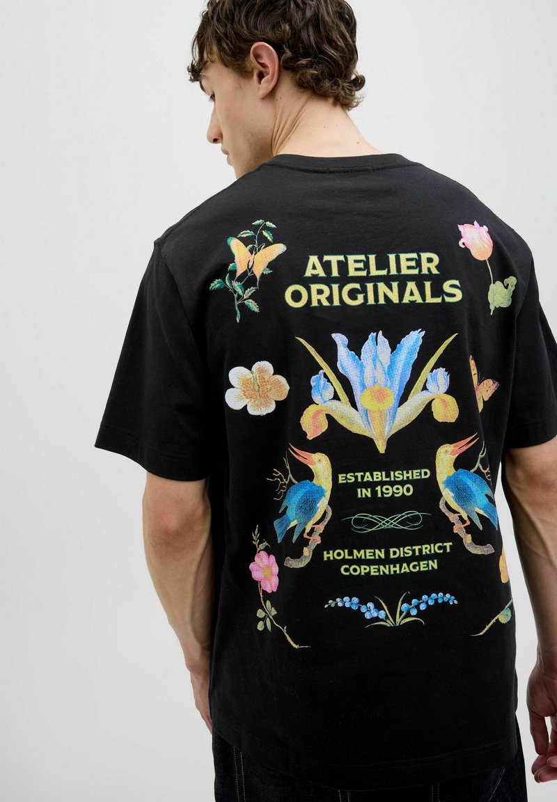 Čierne bavlnené tričko s farebnou grafiku kvetin a vtákov na chrbte, s textom "ATELIER ORIGINALS" a podrobnosťami o mieste.