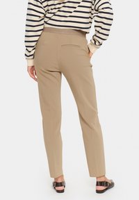 Pantalons beiges ajustés avec une texture lisse, coupe slim et une poche arrière. Portés avec un haut à rayures à longues manches et des sandales brunes.