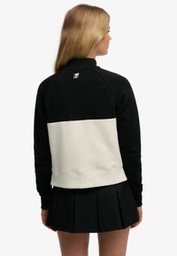 Bluza w kolorze czarno-białym z blokowym wzorem, z prążkowanym kołnierzem i talią, z małym logo na plecach. Połączona z czarną plisowaną spódnicą.