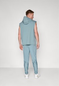 Athletic outfit featuring a sleeveless, hooded top and matching tapered pants in a soft blue color, made from lightweight, smooth fabric.