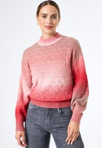 Gebreide trui met een verloop van lichtroze naar rood, met een getextureerd diamanten patroon en geribde boorden en zoom. Gepaard met grijze jeans.