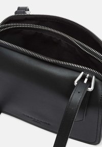 Borsa in pelle nera con due scomparti con cerniera, hardware argentato e tracolla piatta regolabile in pelle. Interno foderato in tessuto.