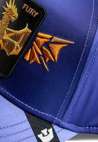 Violetinė kepurė su išsiuvinėtu drakonu ir geometrinėmis oranžinėmis detalėmis, juoda plokštelė su užrašu 'FURY' ir kontrastingais siuvinėjimo elementais.