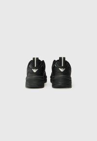 Zwarte sportschoenen met een gestructureerde zool, gebogen vorm en een trekkraag aan de achterkant. Bevat een logo met zilveren accenten op de hiel.