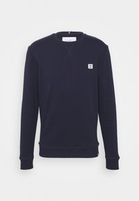 Felpa a maniche lunghe blu navy con collo a giro, polsini e fondo a coste, piccolo logo patch bianco sul petto e etichetta del collo di marca.