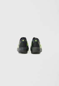 Zwarte sportschoenen met groene accenten, met een soepele textiele bovenkant en een gestructureerde zool, weergegeven vanuit de achterkant.