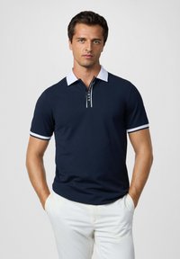 Námorná polo košeľa s bielym golierom a manžetami, s predným zipsom a detailom loga. Hladká textúra a krátke rukávy.