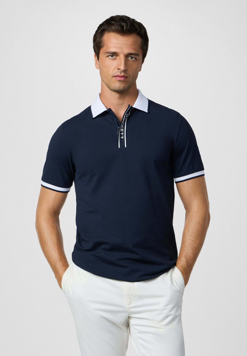 Námorná polo košeľa s bielym golierom a manžetami, s predným zipsom a detailom loga. Hladká textúra a krátke rukávy.