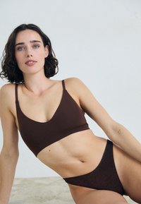 Bralette marron avec un décolleté en V et des bretelles fines, associé à un bas de bikini brillant taille basse assorti. Tissu lisse avec un léger éclat.