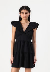 Vestido preto com decote em V, mangas bufantes e saia em camadas. Feito de um tecido suave com uma textura lisa, apresentando um corpete ajustado.