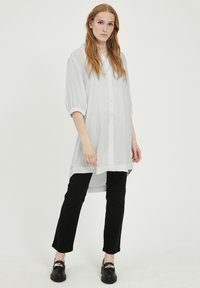 Cămașă albă, supradimensionată, cu guler și mâneci bufante, asociată cu pantaloni negri slim-fit. Textură fină, material ușor.