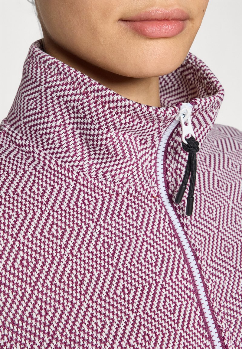 Giacca strutturata con motivo viola e bianco, colletto alto, zip frontale con tirante nero, caratterizzata da un design geometrico su tutta la stoffa.