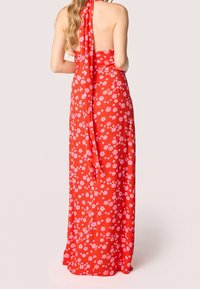 Červené květinové maxi šaty s halter výstřihem a otevřeným zádovým výstřihem; vykazují lehký materiál zdobený růžovými květinovými vzory a volným zavazováním.