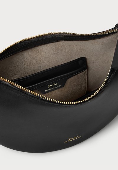 Črna usnjena torbica s ukrivljeno obliko, z zlatim zadrgo in bež semiša notranjostjo. Vključuje prostor za kartice in embosirano logotip.