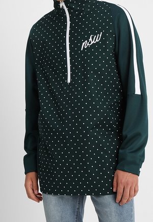 Sudadera verde con puntos blancos, media cremallera y logotipo bordado "nsw". Presenta rayas blancas en las mangas. Tejido suave.