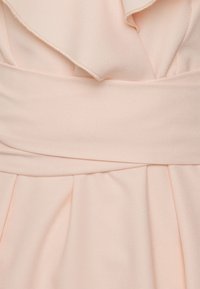 Ljusrosa klänning med en volang halsringning, en slät tygtextur och en bred midja med veck som skapar en flödande look.