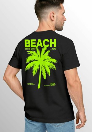 Black cotton t-shirt featuring a neon green palm tree graphic and text on the back. Design includes "BEACH," "Social Club," and other text elements.